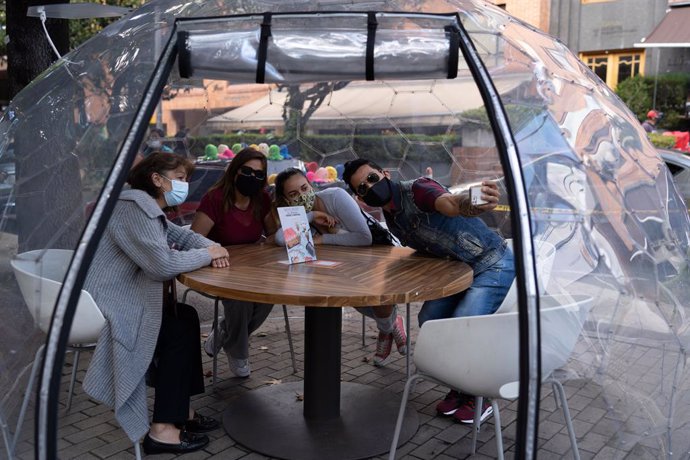 20 December 2020, Colombia, Bogota: A family sits inside a bubble-shaped gazebo installed by a restaurant in Bogota. Several restaurants in the city have installed gazebos to ensure a safe distance between customers. Photo: Natalia Ortiz Mantilla/dpa
