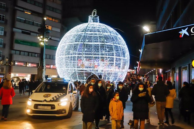 Transeúntes bajo las luces navideñas mientras un coche de Policía vigila la zona, en Vigo, Galicia (España), a 25 de diciembre de 2020. Vigo está cerrada perimetralmente, pero abierta entre el 23 y 25 de diciembre para permitir encuentros familiares.
