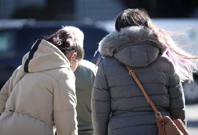 Dos mujeres con abrigo pasean en un día de viento.