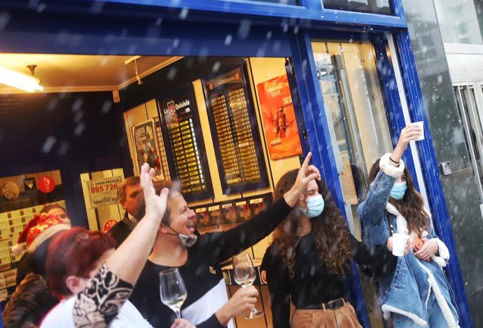 Loteros y clientes de una administración de Lotería brindan después de la celebración del sorteo, en Ferrol (A Coruña)