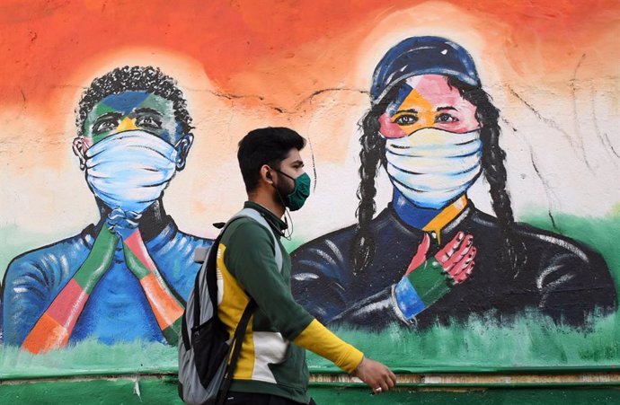 Un hombre con mascarilla delante de un grafiti en India durante la pandemia de coronavirus