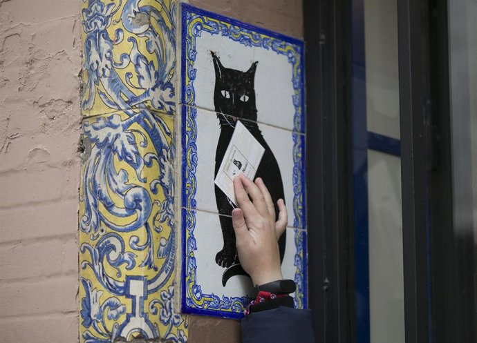 Un niño pasa un boleto de la lotería del Niño por el azulejo de la suerte de la administración de loterías El Gato Negro de Sevilla.
