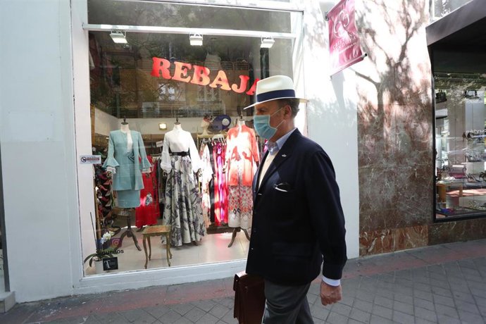 Un hombre protegido con mascarilla pasa junto a una tienda de ropa en la que se anuncian rebajas