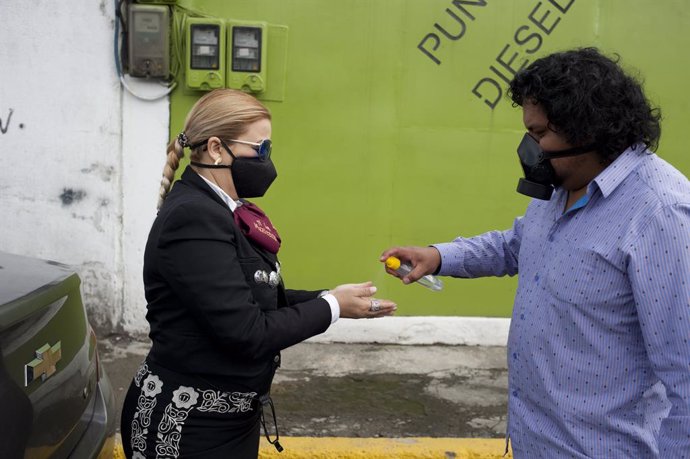 21 June 2020, Ecuador, Quito: A man hands disinfectant to a musician of the Mariachi group "Mariachis a la Mexicana" during the celebrations of the Father's Day, due to the ongoing coronavirus pandemic. Photo: Juan Diego Montenegro/dpa