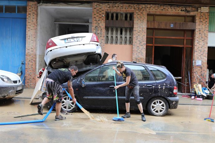 Dos personas trabajan para paliar los efectos de las inundaciones junto a varios coches gravemente dañados en Tafalla (Navarra).