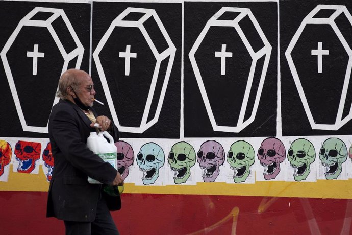 Un hombre camina frente a un mural con ataúdes en Sao Paulo, Brasil.