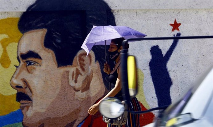 Una mujer camina bajo su paraguas frente a un mural con la imagen del presidente de Venezuela, Nicolás Maduro, en la ciudad de Guacara