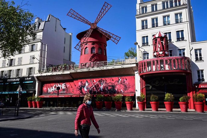 Una mujer con mascarilla pasa frente al Molino Rojo de París