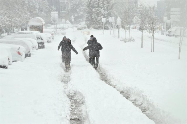 Algunas personas caminan por una calzada completamente cubierta de nieve.