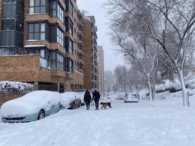 Dos personas pasean con su perro por la calzada completamente cubierta de nieve del Paseo de Extremadura a la altura de Batán en Madrid (España) a 9 de enero de 2021.