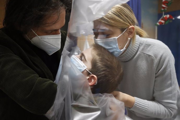 29 December 2020, Italy, Rome: A hospitalized child embraces his parents through a transparent sheet used to prevent the transmission of the COVID-19 at the Department of paediatric rehabilitation and developmental disabilities of IRCCS at the San Raffa