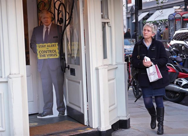Una mujer pasa junto a un cartel de Boris Johnson concienciando de los riesgos del coronavirus