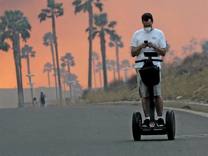 A man usues his cell phone while riding a Segway November 15, 2008 as the glow from a fire is seen in the distance in Yorba Linda, California.
