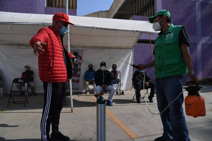 Un hombre es 'desinfectado' antes de ingresar a un establecimiento en el que se rellenan botellas de oxígeno.