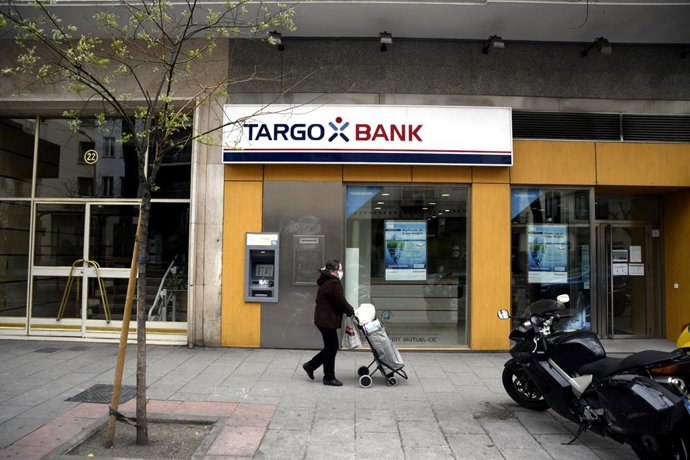Una mujer protegida con mascarilla pasa delante de una oficina Targobank.