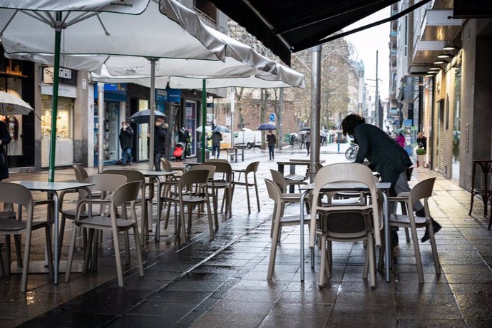 Una persona limpia las mesas en la terraza de un establecimiento de Vitoria