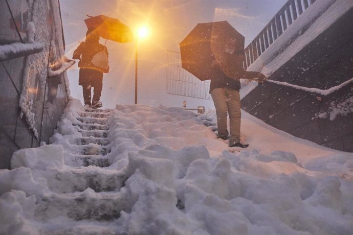 Dos personas bajan una escalera de una estación de metro cubierta de nieve tras el paso de la borrasca Filomena, en Madrid (España) a 9 de enero de 2021.La borrasca Filomena golpea con fuerza la capital, en la que se han cerrado al tráfico circunvalacio