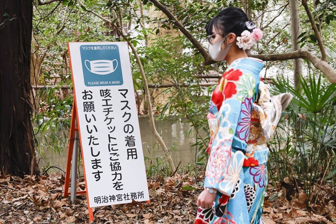 11 January 2021, Japan, Tokyo: A Japanese girl dressed in colorful kimono walks past a signboard saying 'Please wear a mask' at the Meiji Shrine during the Coming of Age Day holiday. The Coming of Age Day (Seijin-no-Hi) is a holiday to congratulate and 