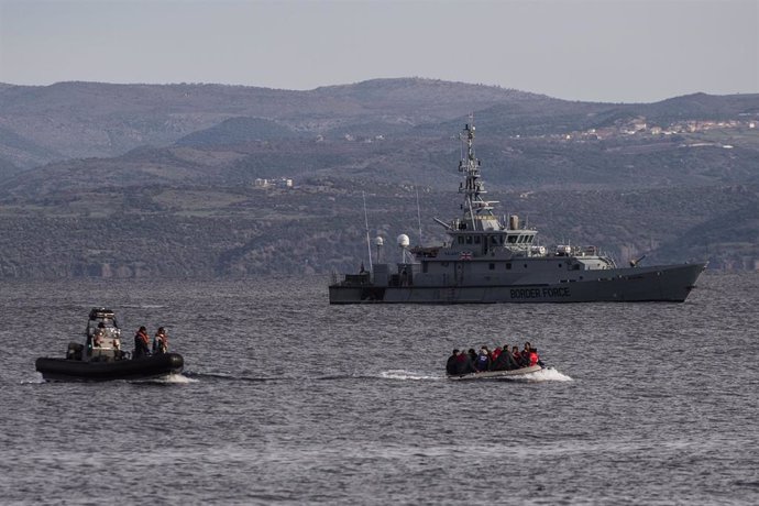 Una embarcación con migrantes llega a la isla griega de Lesbos, frente al barco británico 'HMC Valiant', parte de la misión Frontex