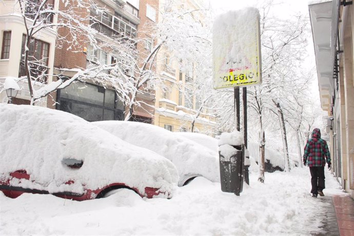 Una persona pasea por una céntrica calle cubierta de nieve junto al acceso de un colegio en Madrid