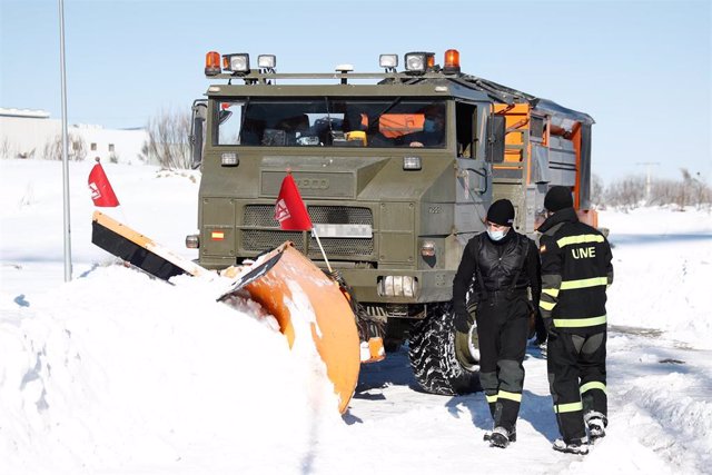Una excavadora de la Unidad Militar de Emergencias (UME) y dos militares durante la limpieza de una de las carreteras llenas de nieve.