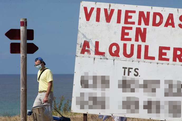 Un home camina al costat d'un cartell d'habitatges de lloguer. A Mariña, Galícia (Espanya), 26 de juliol del 2020.