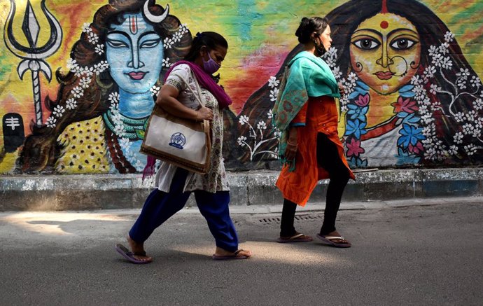 Dos mujeres pasean frente a un mural en India llevando mascarilla debido a la crisis sanitaria provocada por el coronavirus.