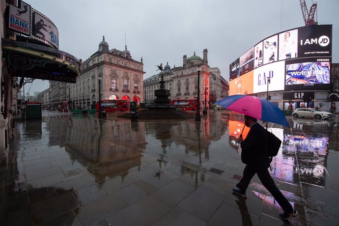 14 January 2021, England, London: A man with an umbrella walks along the empty Piccadilly Circus in London during England's third national lockdown to curb the spread of coronavirus. Photo: Dominic Lipinski/PA Wire/dpa