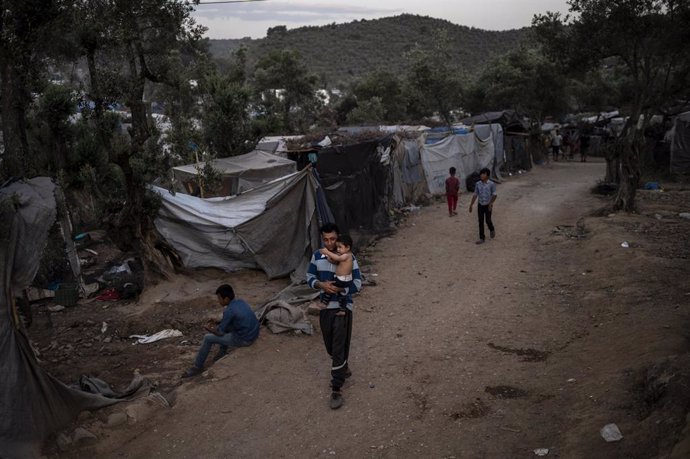 21 June 2020, Greece, Lesbos: A refugee walks with a child through a temporary camp next to the refugee Camp Moria on the island of Lesbos. Greece announced on Saturday another extension of the coronavirus lockdown on its teeming migrant camps. Photo: A