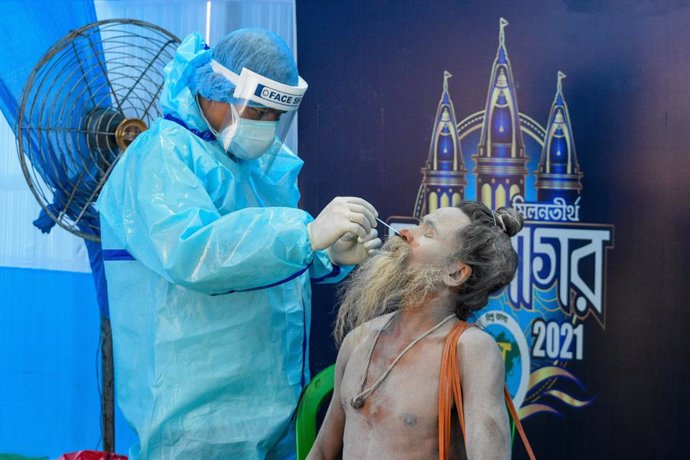 09 January 2021, India, Kolkata: A medical worker wearing protective clothing takes a nasal swab from a religious man for a Coronavirus test. The government set up a corona testing centre at a campsite to offer free testing to religious people who visit