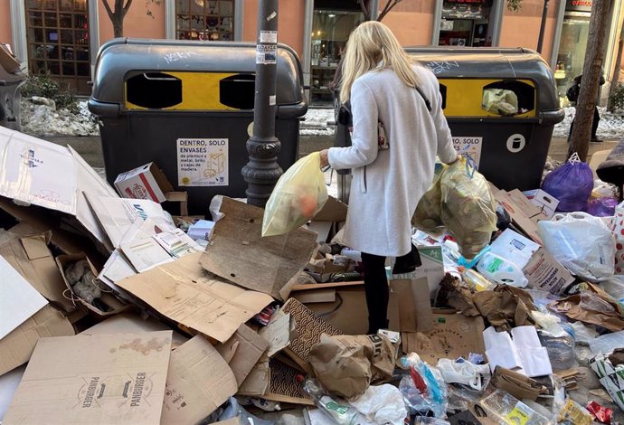 Una mujer tira dos bolsas de basura donde hay acumuladas otras tantas decenas de bolsas en un punto de Alonso Martínez