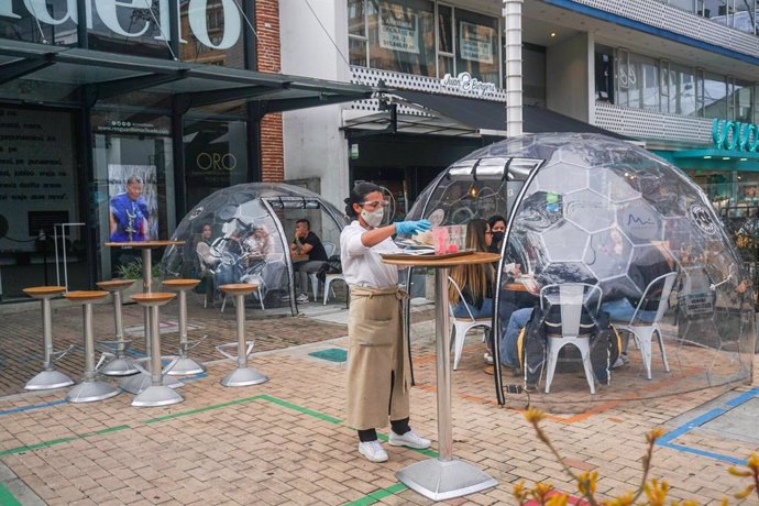 26 December 2020, Colombia, Bogota: A waitress serves food to customers who sit inside a capsule as a biosecurity measure due to the spread of coronavirus (COVID-19). Photo: Daniel Garzon Herazo/ZUMA Wire/dpa