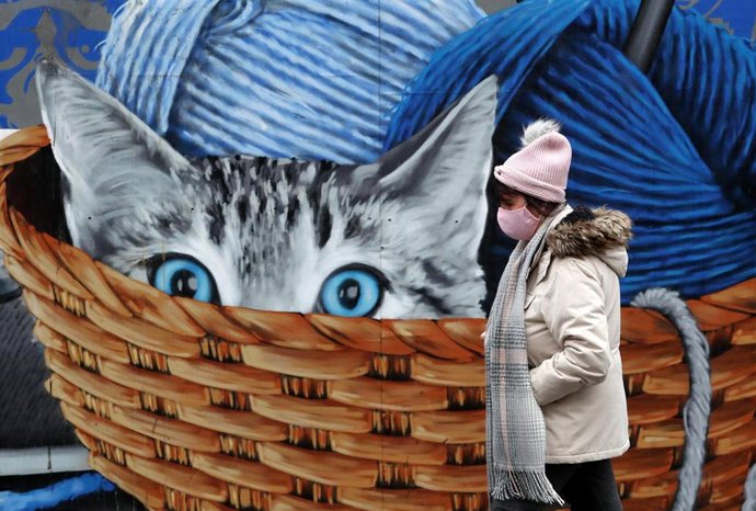 Una mujer con mascarilla junto a un mural con un gato en Glasgow