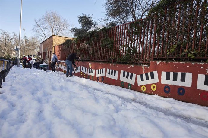 Varios familiares colaboran en la limpieza del hielo y la nieve en las inmediaciones del colegio Amadeo Vives tras la gran nevada por el paso de la borrasca 'Filomena', en Madrid, (España), a 16 de enero de 2021. 