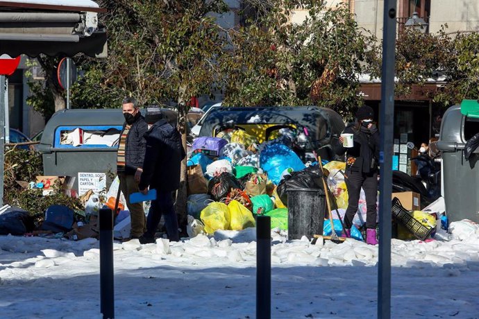 Dos personas pasan al lado de un cúmulo de residuos en una vía como consecuencia de la nevada provocada por la borrasca Filomena.