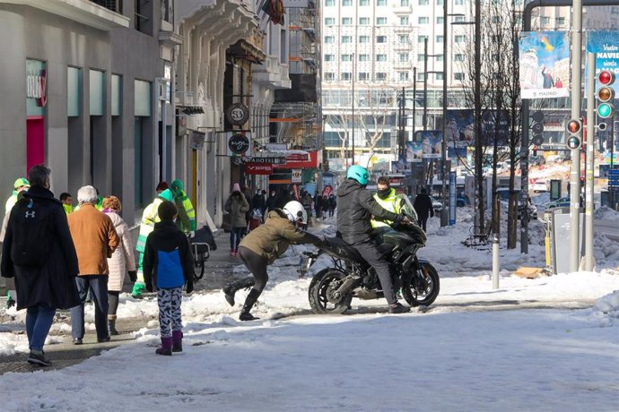 Un hombre empuja a otro en una moto atascada por el hielo en una calle céntrica de la capital, en Madrid (España), a 13 de enero de 2021. Madrid sigue cubierto de nieve cinco días después de la gran nevada provocada por el paso de la borrasca Filomena