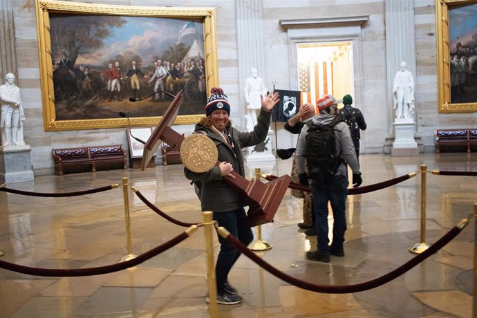 Uno de los simpatizantes de Donald Trump que asaltaron el Capitolio se lleva un atril mientras saluda
