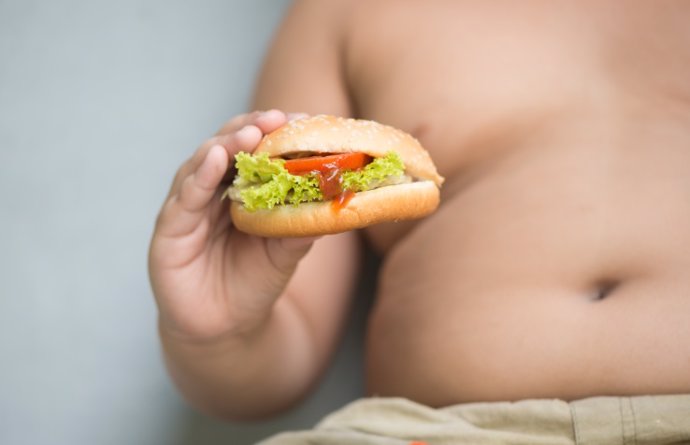 Imagen de archivo de un niño con obesidad mostrando una hamburguesa.