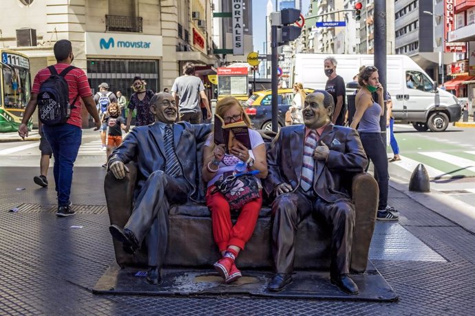 03 December 2020, Argentina, Buenos Aires: A woman reads a book while sitting on a bench next to two status. Photo: Roberto Almeida Aveledo/ZUMA Wire/dpa