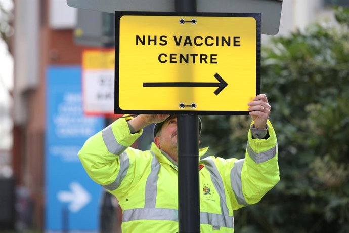 18 January 2021, United Kingdom, London: A community worker hangs a sign pointing the way to the National Health Service (NHS) Corona vaccination centre at the Olympic Office Centre in Wembley, as ten further mass vaccination centres open in England wit