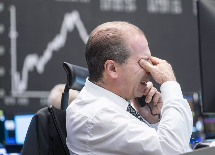 04 November 2020, Hessen, Frankfurt: A trader sits in the trading room of the Frankfurt Stock Exchange in front of his monitors, as the Dax curve can be seen in the background. Photo: Frank Rumpenhorst/dpa