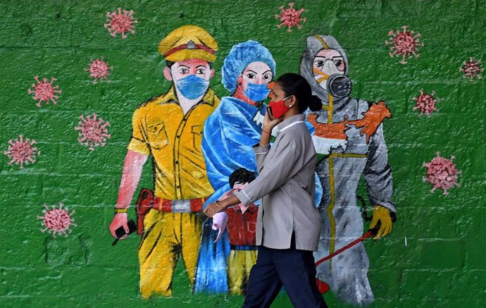 Una mujer con mascarilla frente a un mural en India durante la pandemia de coronavirus