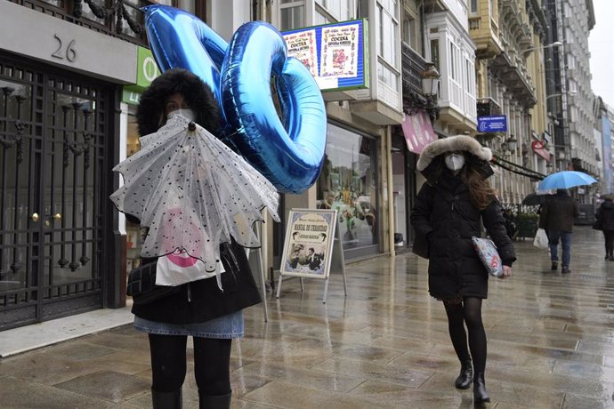 Transeúntes caminan protegidos por una vía de A Coruña, Galicia (España), a 20 de enero de 2021. El temporal de nieve y posterior frío provocado por la borrasca 'Filomena' terminará este martes cuando ésta pase el testigo a un nuevo frente, bautizado po