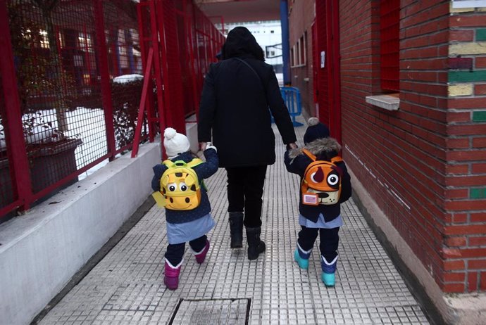 Un familiar lleva de la mano a dos alumnos del colegio Arcangel Rafael el día de la reapertura de los centros educativos tras la gran nevada registrada por el paso de Filomena, en Aluche, Madrid, (España), a 20 de enero de 2021. El paso de la borrasca