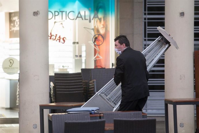 Un camarero recoge una lámpara de calor de la terraza de un restaurante.