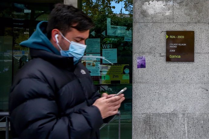 Un joven mira su móvil delante de una sucursal de Bankia en Collado Villalba.