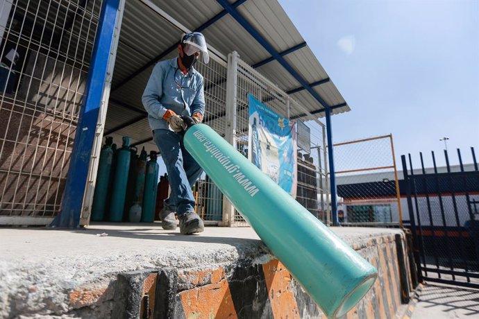 21 January 2021, Mexico, Queretaro: A worker carries an oxygen cylinder inside a factory while people line up to buy oxygen for their relatives infected with the coronavirus disease (COVID-19). Mexico faces a shortage of oxygen tanks and a fourfold rise