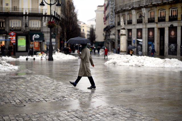 Una persona camina protegida por la Puerta del Sol el mismo día de la llegada del temporal ‘Gaetán’
