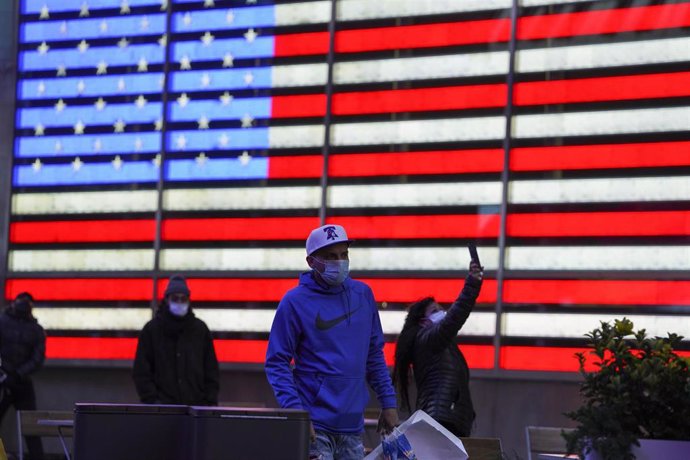 Personas con mascarilla frente a un cartel luminoso con la bandera de Estados Unidos en Nueva York