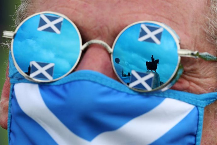 Un hombre con mascarilla y gafas de la bandera escocesa durante una manifesatción independentista en Bannockburn. En las gafas se ve reflejada una estatua ecuestre de Robert Bruce